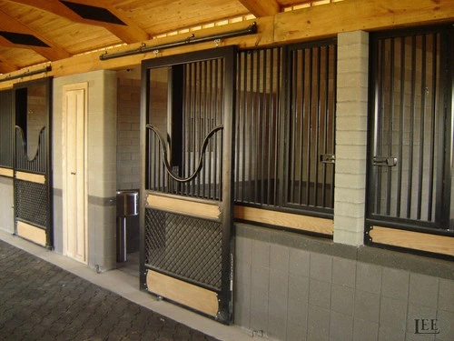 Gray metal stall fronts with vertical bars and wire mesh panels along bright white barn aisle