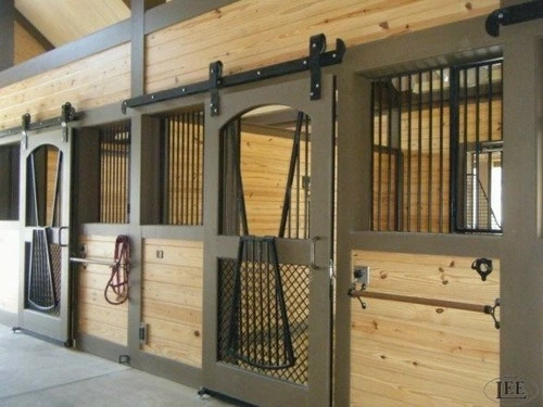 Dark gray metal sliding stall door with vertical bars and wire mesh panel, brown horse visible inside barn aisle