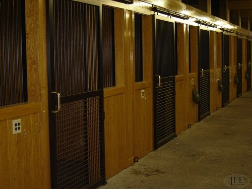 Row of dark wood stalls with wire mesh upper sections in dimly lit aisle