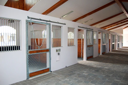 White barn interior with orange-trimmed sliding stall doors along aisle
