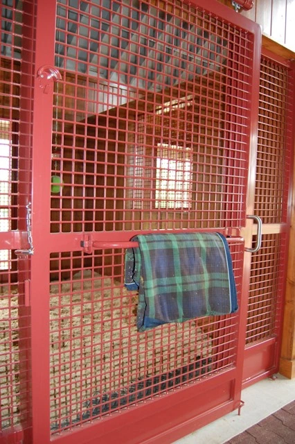 Red wire mesh stall wall with plaid horse blanket draped over edge