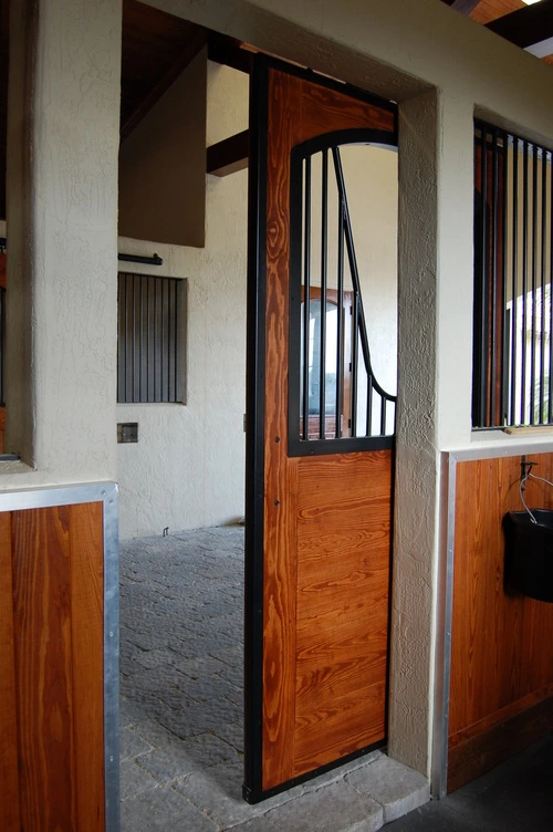 Open stall door with dark wood frame and leather halter hanging outside
