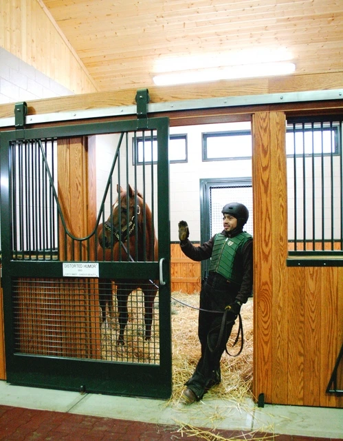 Green-dressed handler with horse in open stall doorway