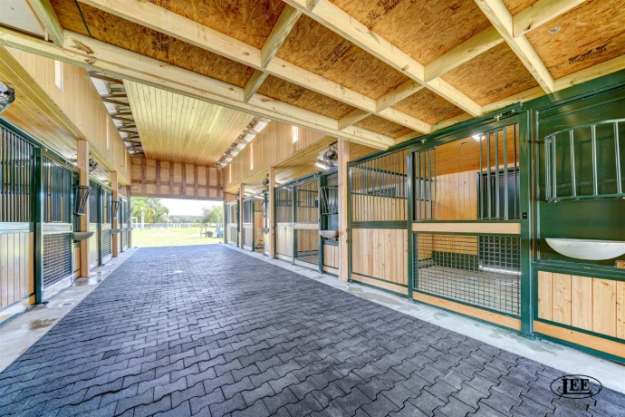 Covered outdoor barn aisle with forest green stall fronts and natural pine lower panels