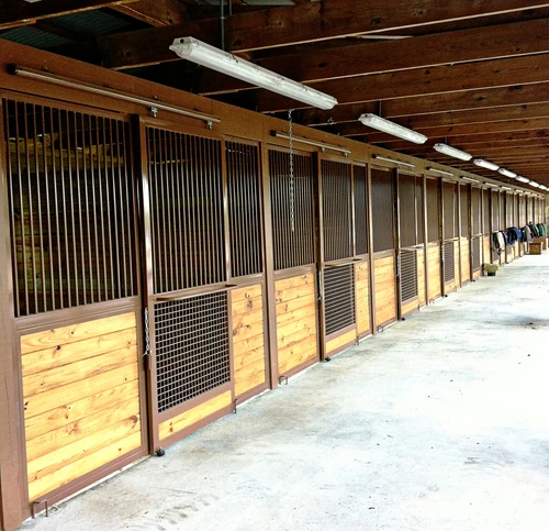 Long barn aisle with natural pine stall fronts, black vertical bar upper grills and exposed wood ceiling