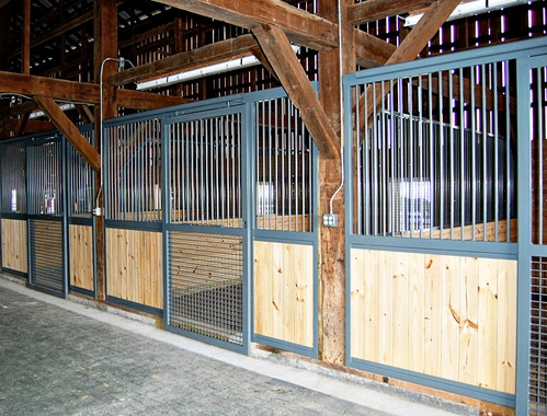 Timber-frame barn aisle with galvanized metal and natural wood stall fronts with wire mesh panels