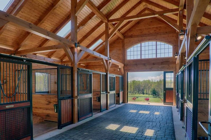 Timber-frame barn aisle with black metal stall fronts, natural wood lower panels and large arched window