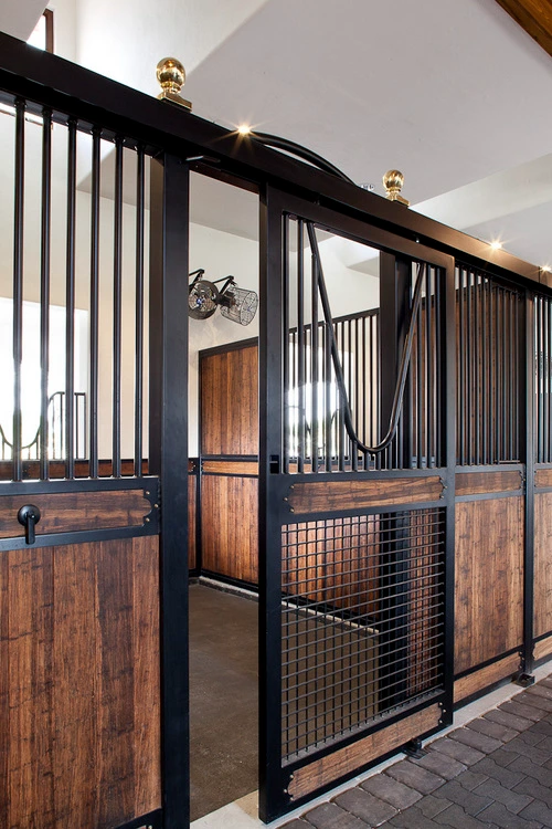 Black metal stall front with natural wood lower panel, wire mesh door and bridle hanging outside