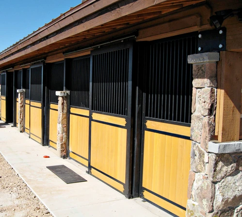 Black metal stall fronts with bright yellow lower panels and wire mesh sections in covered exterior barn