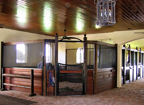 Luxury barn corner with mahogany stall fronts, wire mesh panels, upholstered seating and ornate chandelier
