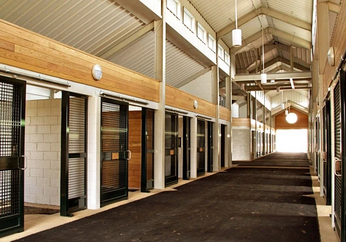 Long modern barn aisle with black metal stall fronts, natural wood lower panels and industrial pendant lighting