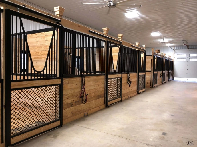 Modern barn aisle with black metal stall fronts, natural pine lower panels, wire mesh doors and pendant lights