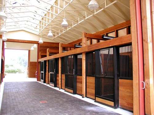 Timber-frame barn aisle with black metal stall fronts, natural pine lower panels under burgundy wood ceiling