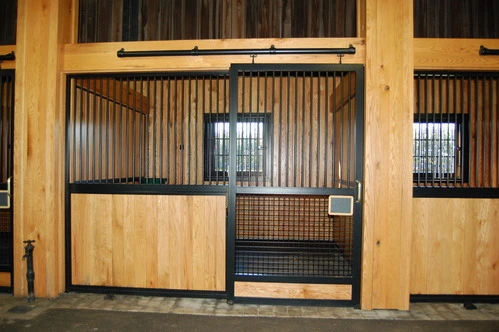 Natural pine stall fronts with black metal vertical bar upper grills and wire mesh window panels in bright barn