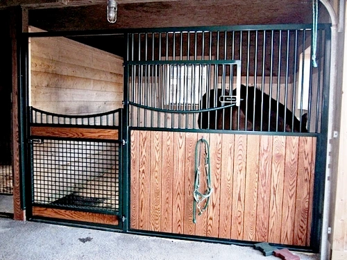 Black metal stall front with natural pine lower panel featuring decorative carved design and rope halter hanging