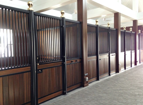 Dark mahogany stall fronts with black vertical bar upper grills in bright modern barn aisle with white ceiling