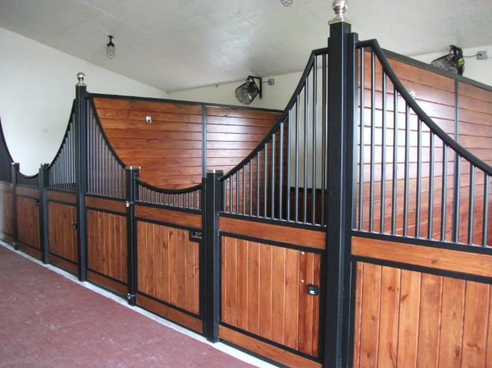 Black metal curved stall fronts with mahogany lower panels and vertical bar upper grills in elegant barn aisle