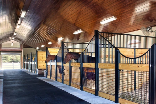 Black metal stall fronts with natural pine lower panels and wire mesh sliding doors in dimly lit barn corridor