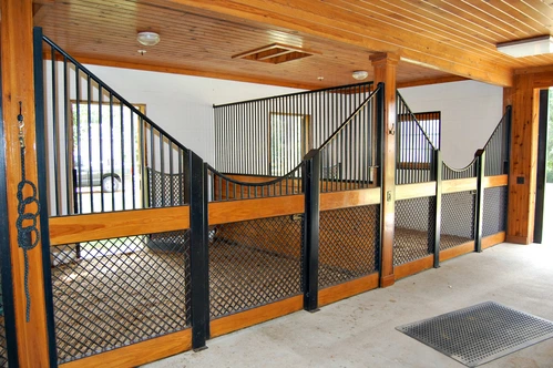 Natural pine stall fronts with black metal vertical bar upper grills and wire mesh lower sections in bright barn