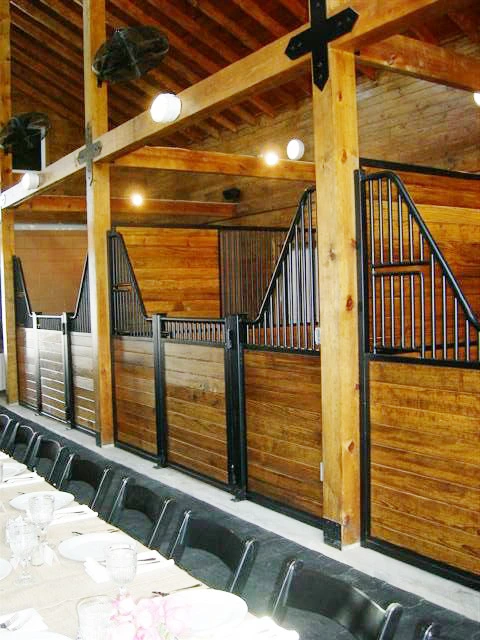 Black metal stall fronts with natural pine lower panels and vertical bar upper grills along barn corridor