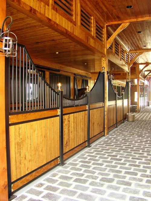 Natural pine stall fronts with black metal vertical bar upper grills and decorative gold finials in bright barn