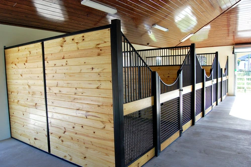 Natural pine stall fronts with black metal vertical bar upper grills and decorative rope swags in white barn