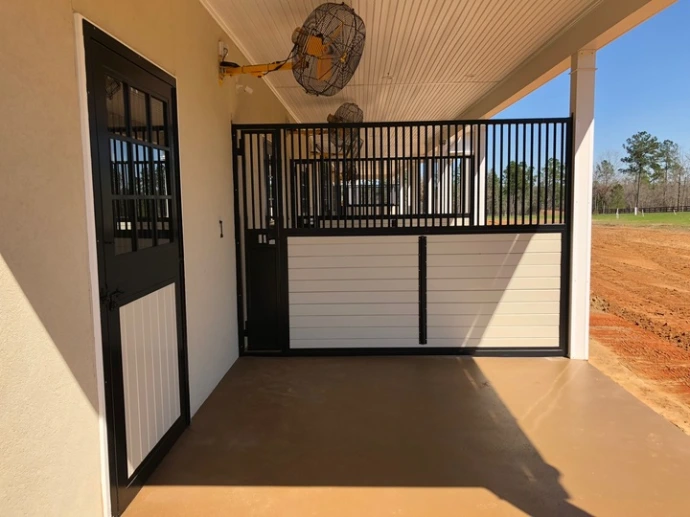 Dark wood stall fronts with black vertical bar upper grills and tan lower sections in covered barn aisle