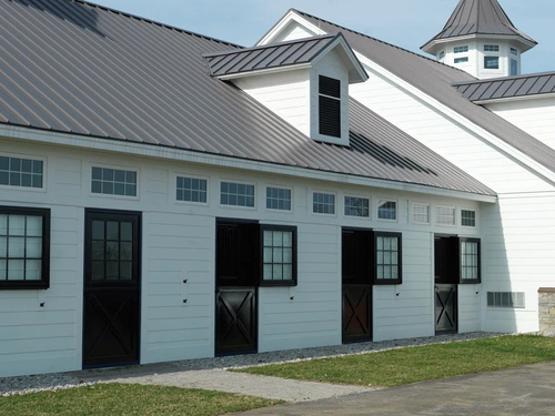 White painted modern barn with multiple black-trimmed stall openings and row of windows