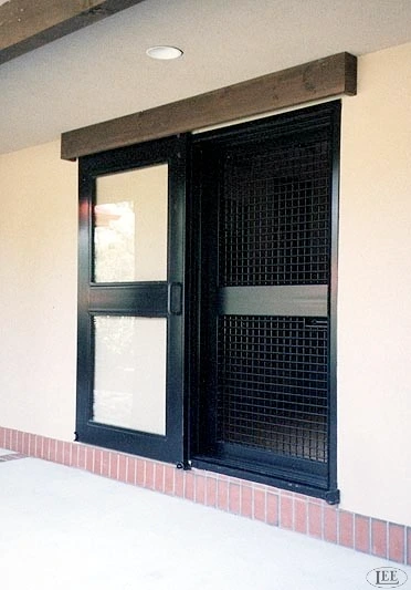 Black metal door with mesh upper panel and solid lower section on cream stucco wall