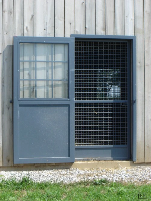 Slate blue metal door with multi-pane window upper section and mesh lower panel on cream wall