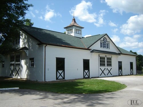 White painted barn with green roof, cupola, and multiple black X-pattern stall doors