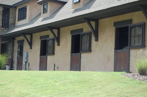 Cream colored barn with covered walkway featuring multiple natural wood Dutch doors and dark upper sections
