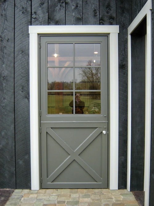 Gray metal door with X-brace diagonal pattern on dark charcoal vertical siding
