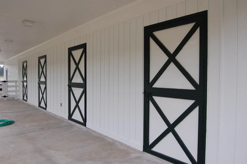 White barn aisle with three black X-pattern doors spaced along length