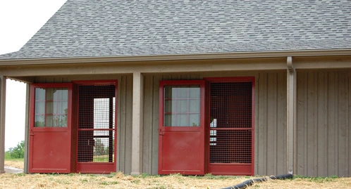 Tan barn with two burgundy doors featuring mesh upper panels and multi-pane windows