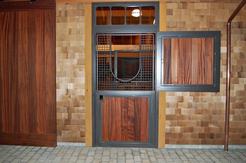 Rich mahogany sliding door with wire mesh panel and decorative horseshoe on natural stone and wood wall
