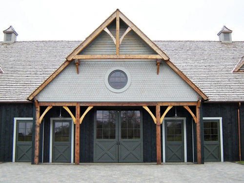 Modern timber-frame barn with black exterior, white trim and arched stall openings with circular window