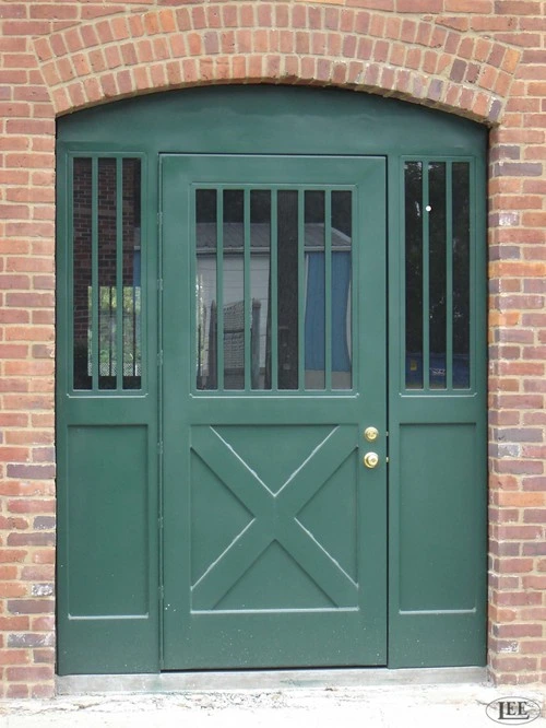 Sage green double doors with vertical bar grills and diagonal X-brace lower panels on red brick