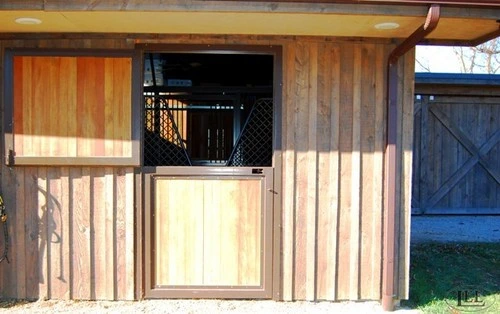 Natural wood vertical siding barn with Dutch door featuring corrugated metal upper grill section