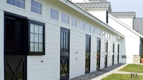 Modern white barn exterior with black X-pattern Dutch doors along length of building