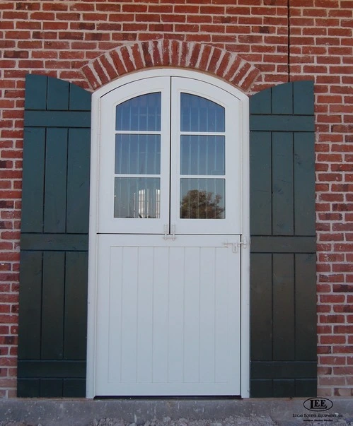 Red brick barn exterior with dark green board-and-batten Dutch doors flanking white French door entry