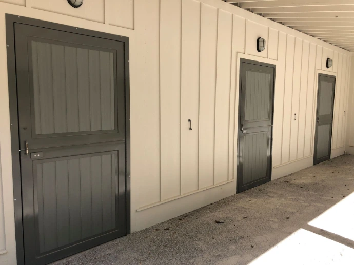 Gray painted vertical plank Dutch doors on white barn interior with concrete floor