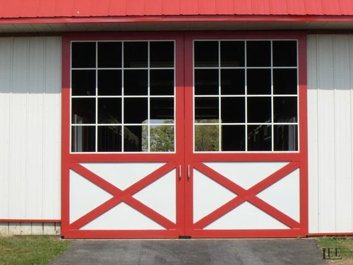 Red barn sliding doors with white X-pattern design and multi-pane windows on white metal siding