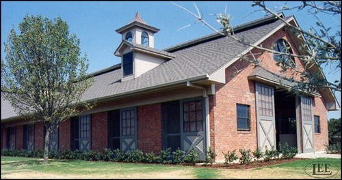 Red brick barn with arched stall openings and black X-pattern sliding doors