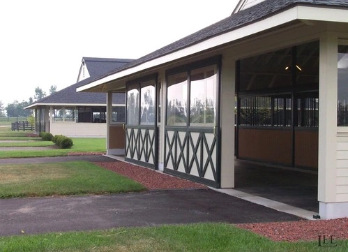 Covered barn aisle with white columns and brown wood stall doors with X-pattern design