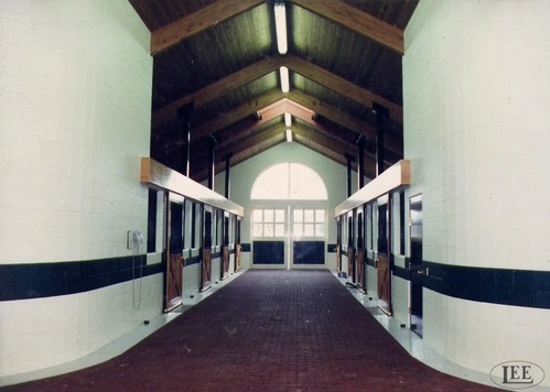 Interior barn aisle view with white walls and black-trimmed stall fronts