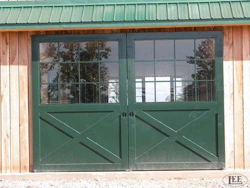 Natural wood barn with sage green double doors featuring X-pattern and upper glass panels