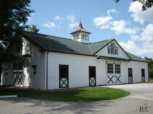 White painted barn with green roof and black X-pattern stall doors along side