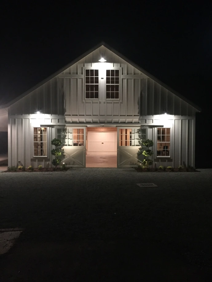 Dark gray barn exterior with illuminated garage-style openings at night