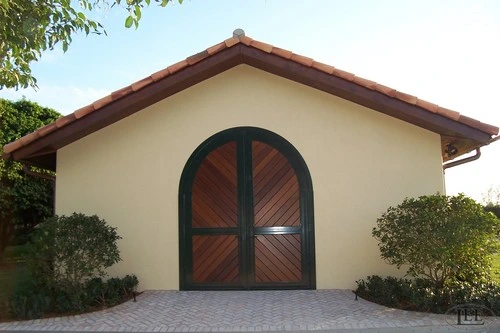 Cream stucco building with large arched double doors featuring diagonal wood planks and dark green frame